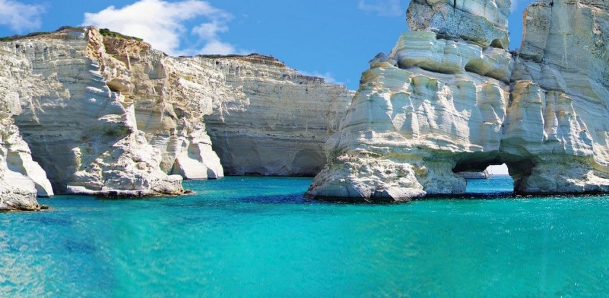 a body of water with large rocks in the background with Milos in the background