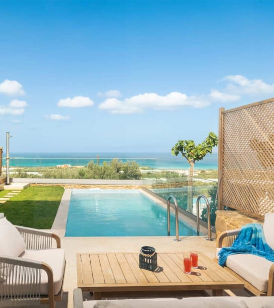 a pool with a deck and chairs by it and a beach in the background