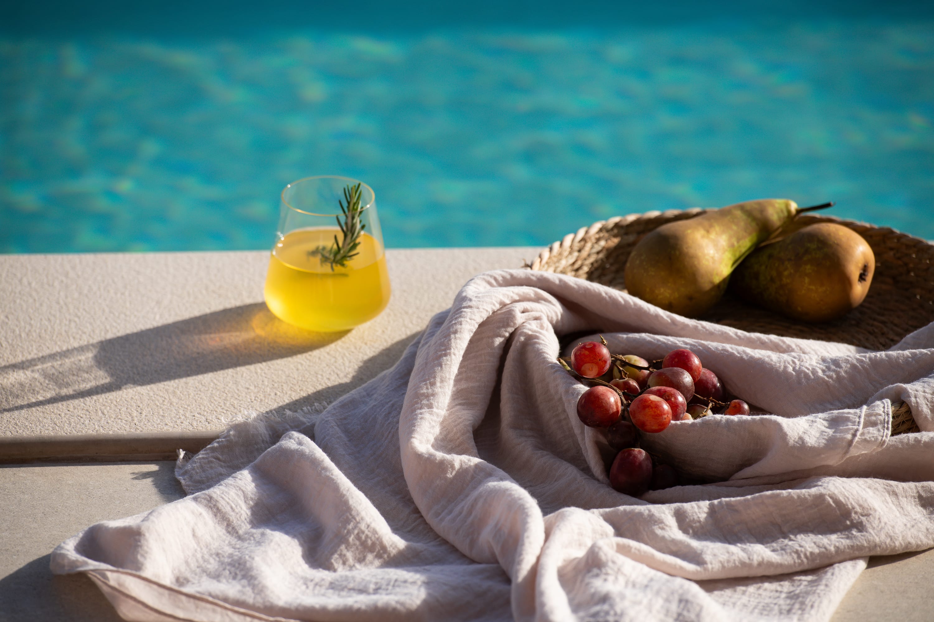 a hand holding a bottle of oil and fruit on a beach