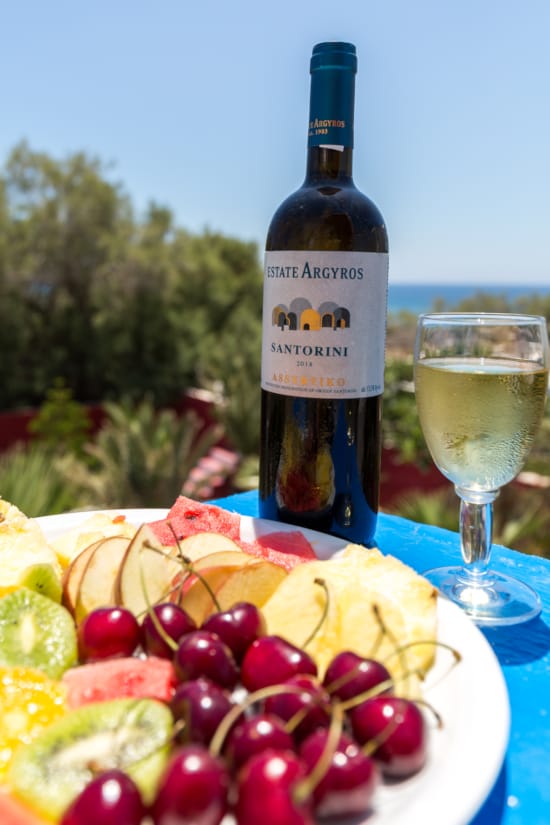 a bottle of wine next to a plate of fruit and a glass of wine
