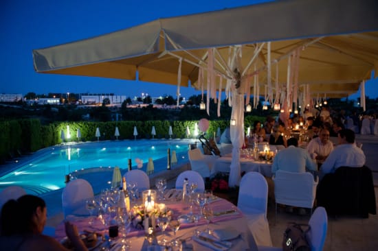 a large group of people sitting at a table with a pool and chairs