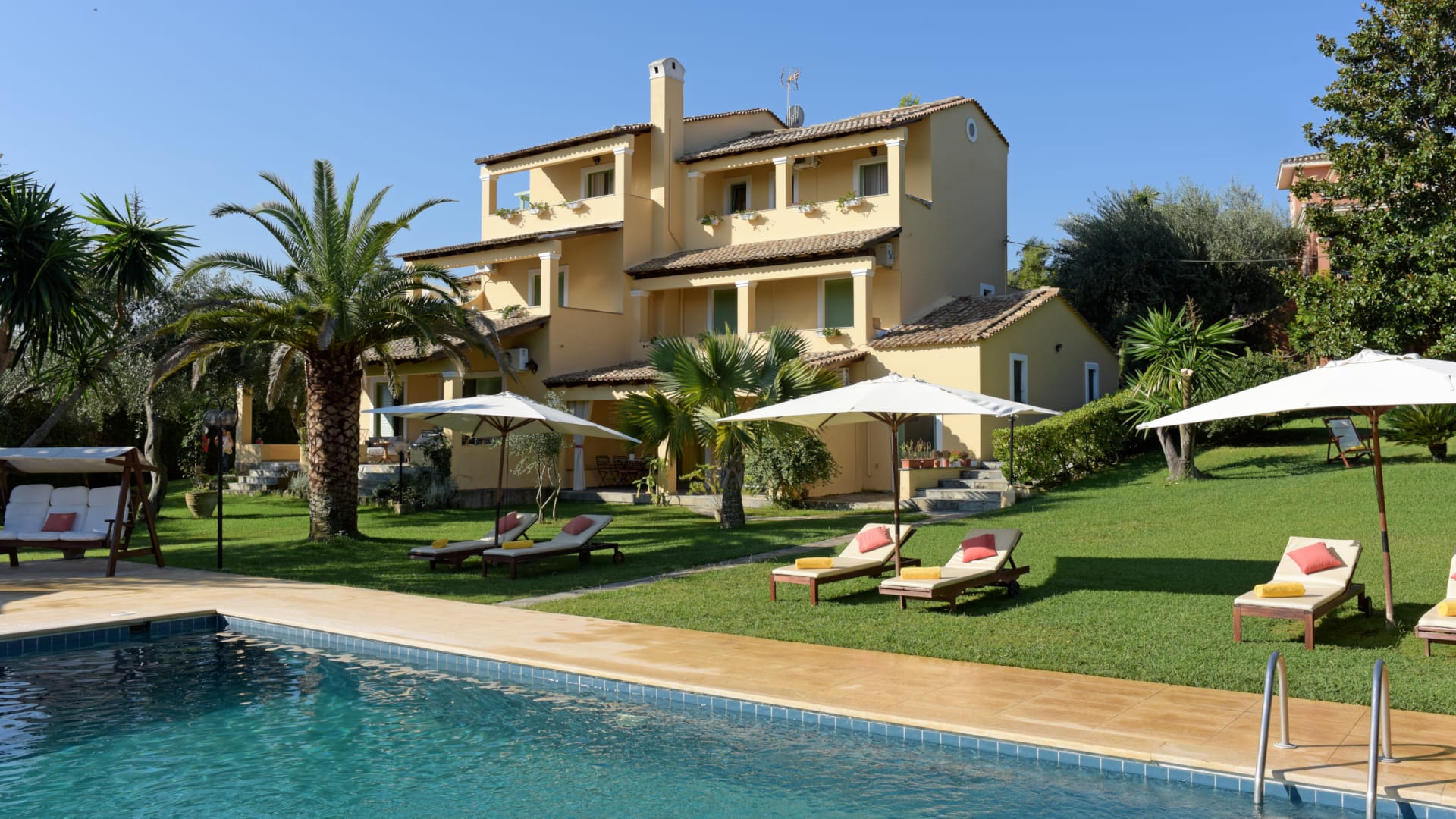 a pool with lounge chairs and umbrellas by a house