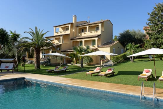 a pool with lounge chairs and umbrellas by a house