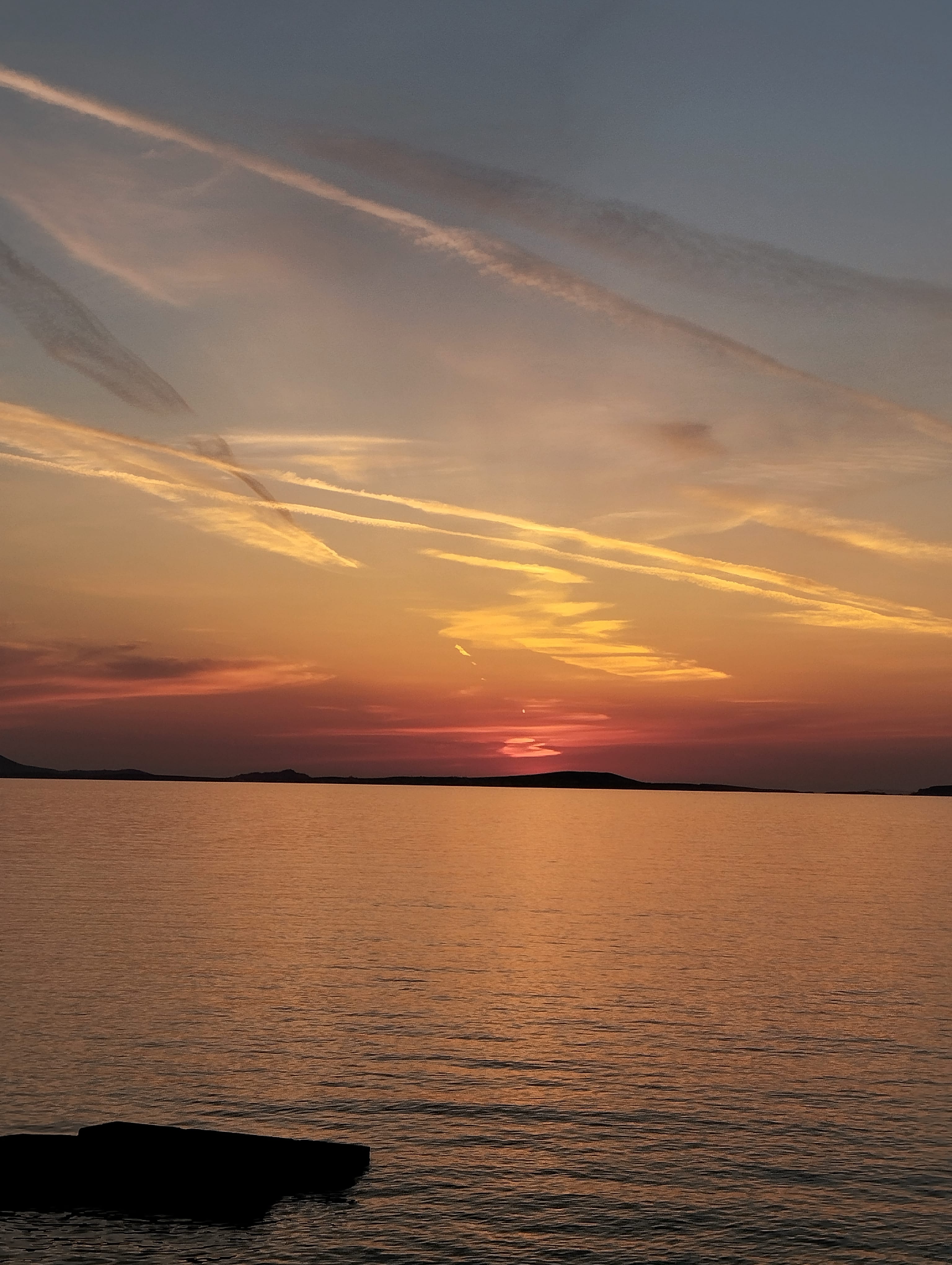 a body of water with a rock in it and a sunset in the background