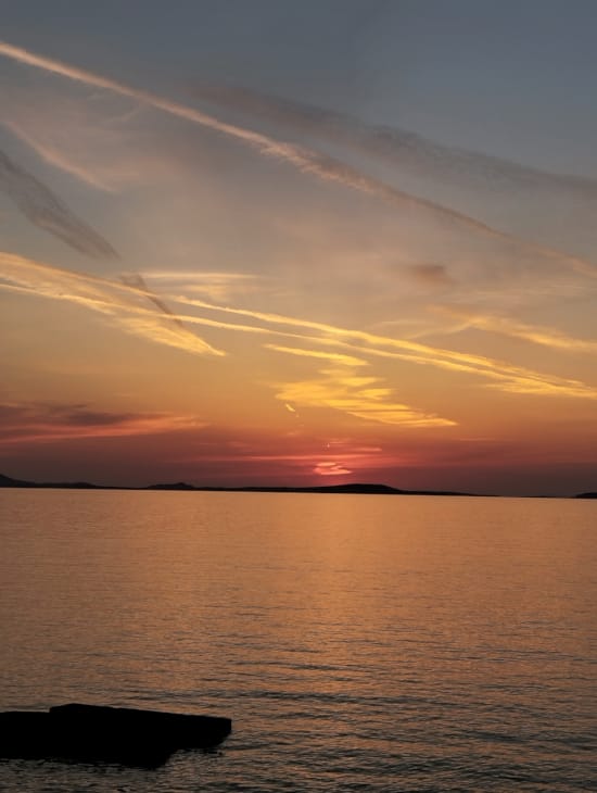 a body of water with a rock in it and a sunset in the background