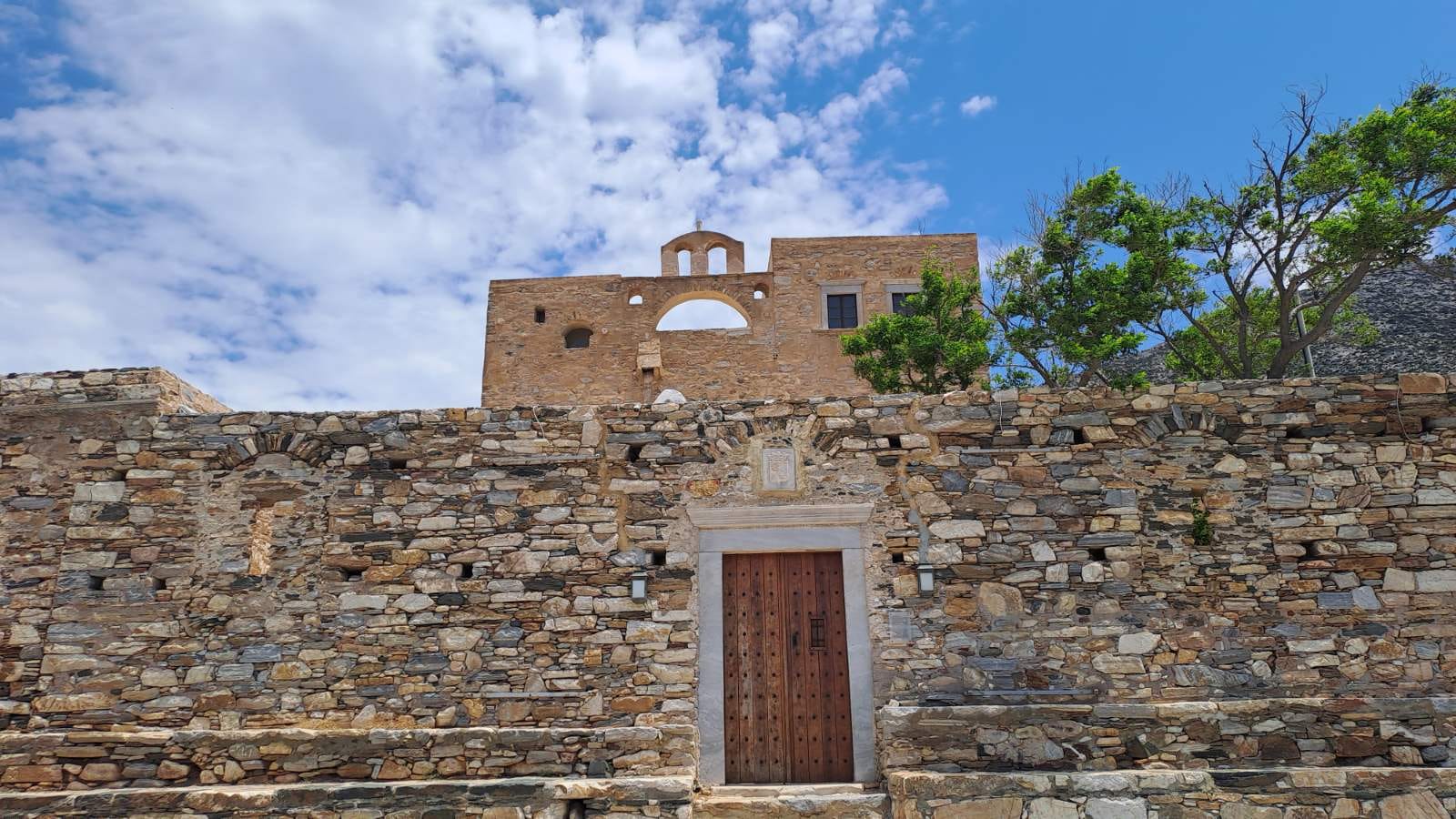 a stone wall with a door and a building in the background