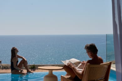 a man and woman sitting at a table with a book and a body of water in the background