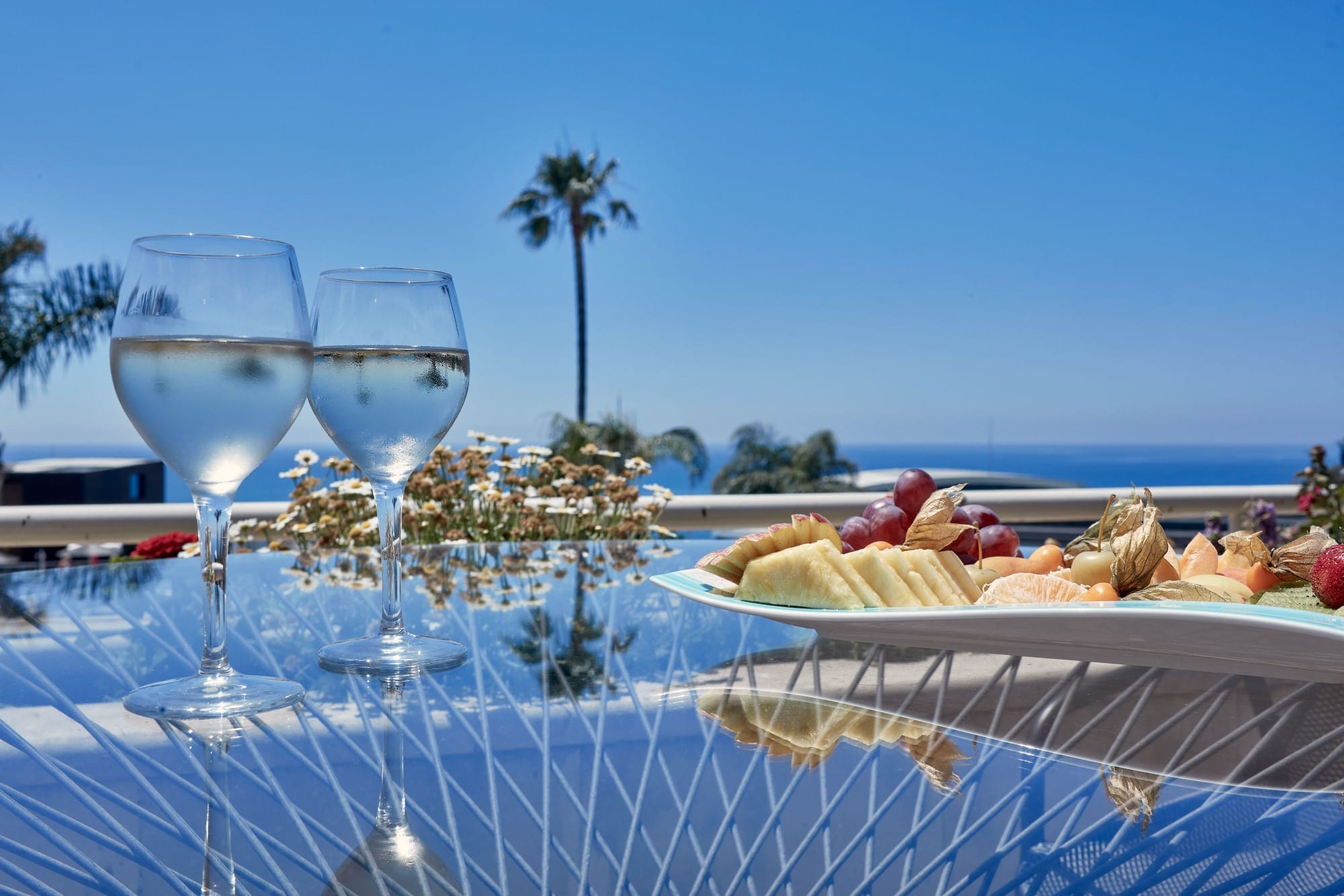 a couple of wine glasses next to a pool with food and palm trees