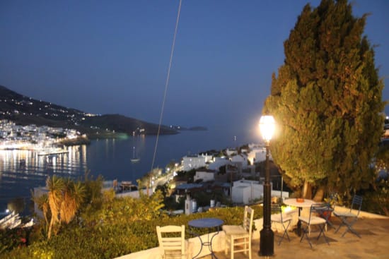 a patio with tables and chairs and a tree with a body of water in the background