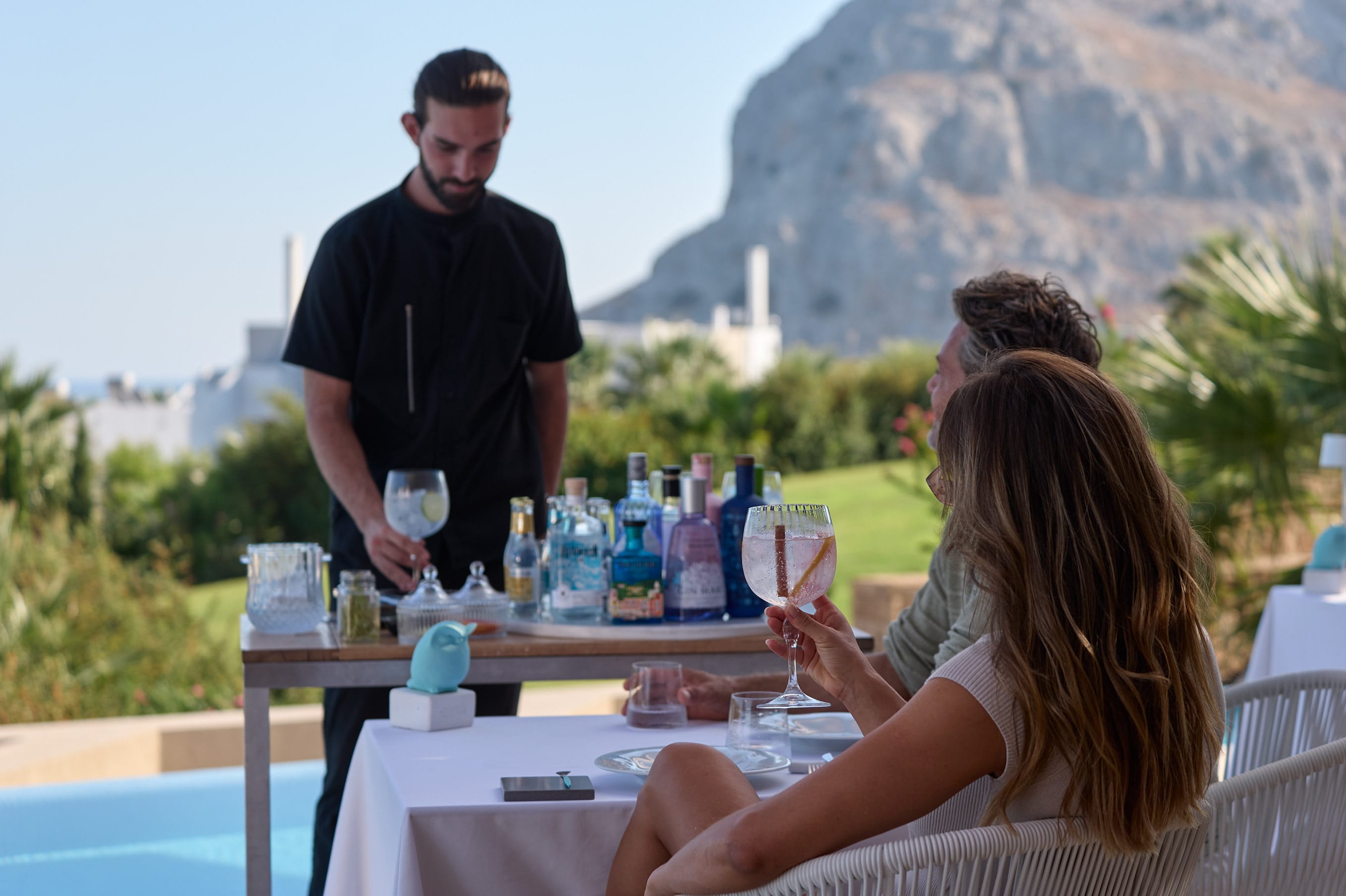 a group of people sitting at a table with drinks and a mountain in the background