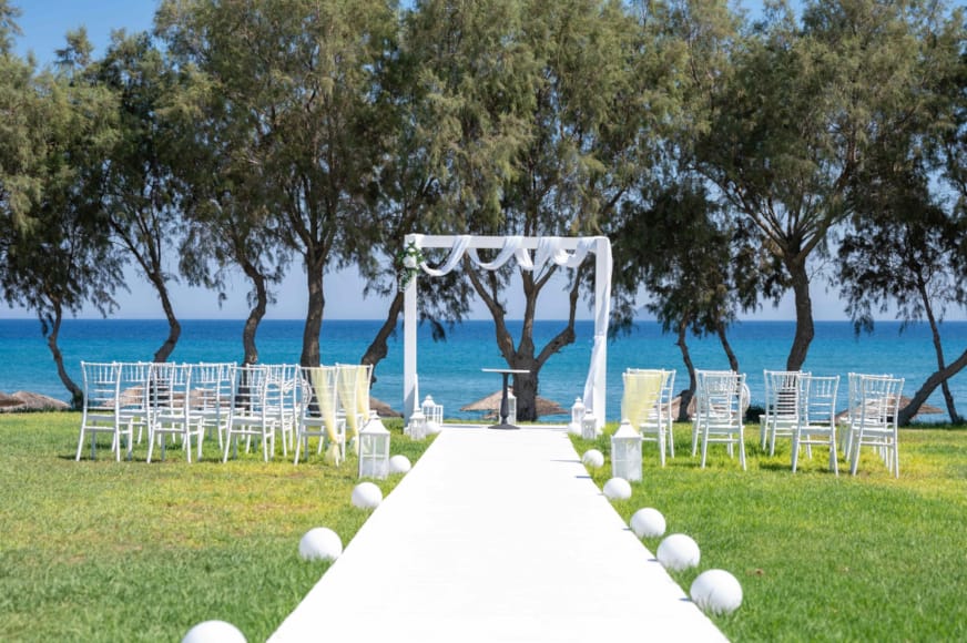 a table set up with white chairs and a white tablecloth with a white table and trees and