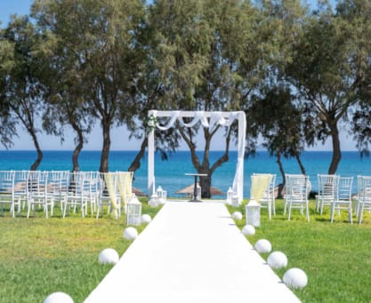 a table set up with white chairs and a white tablecloth with a white table and trees and