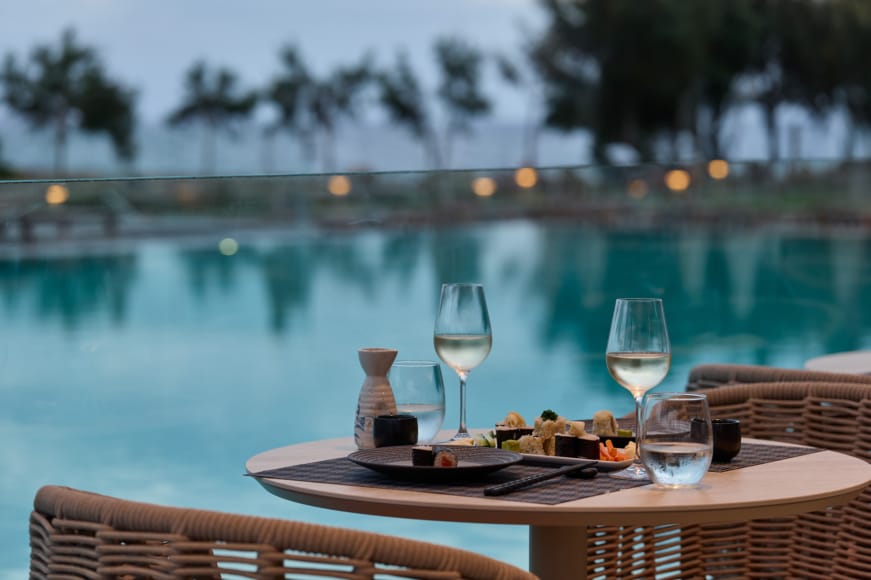 a table with glasses of wine on it by a pool