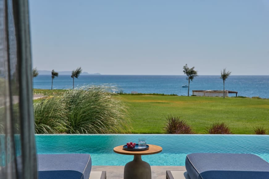 a pool with a table and chairs by a grass field and a body of water