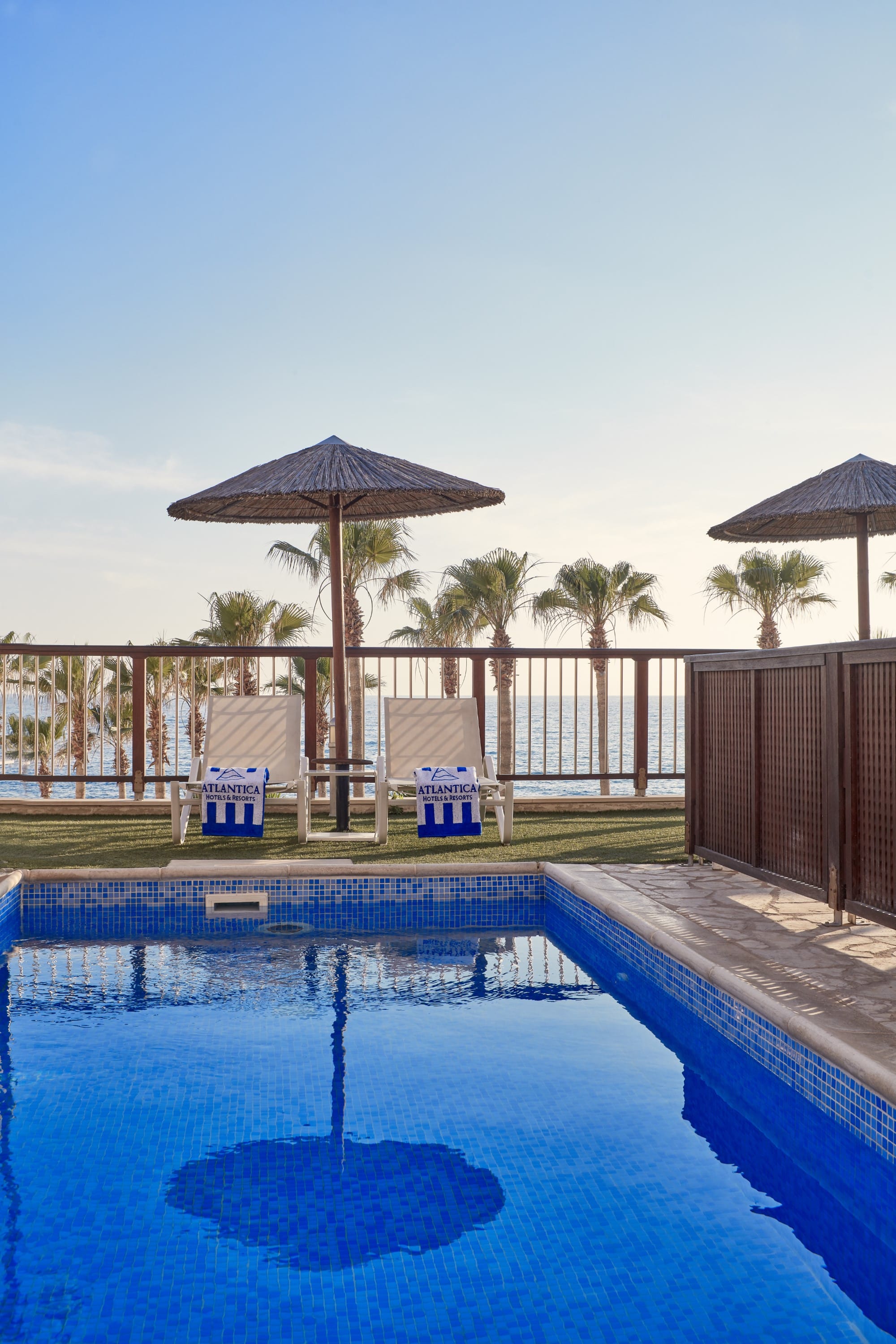 a pool with chairs and umbrellas by a fence and trees