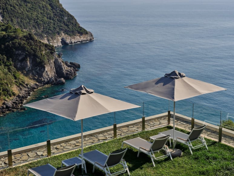 a group of chairs and umbrellas on a grassy hill by the water