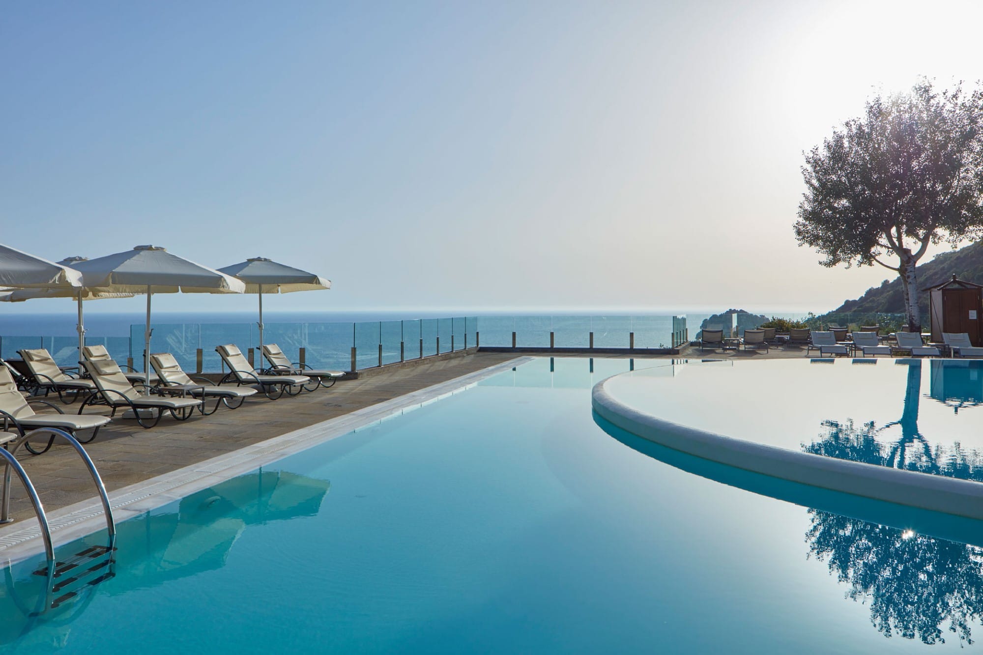a pool with chairs and umbrellas by a beach