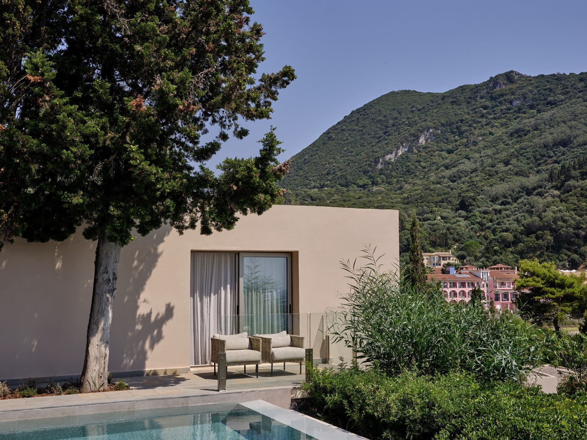 a pool and a tree by a house with a hill in the background