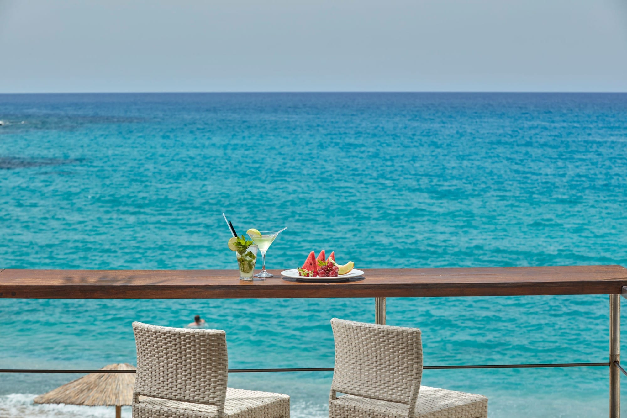 a table with chairs and a plate of fruit on it by the water