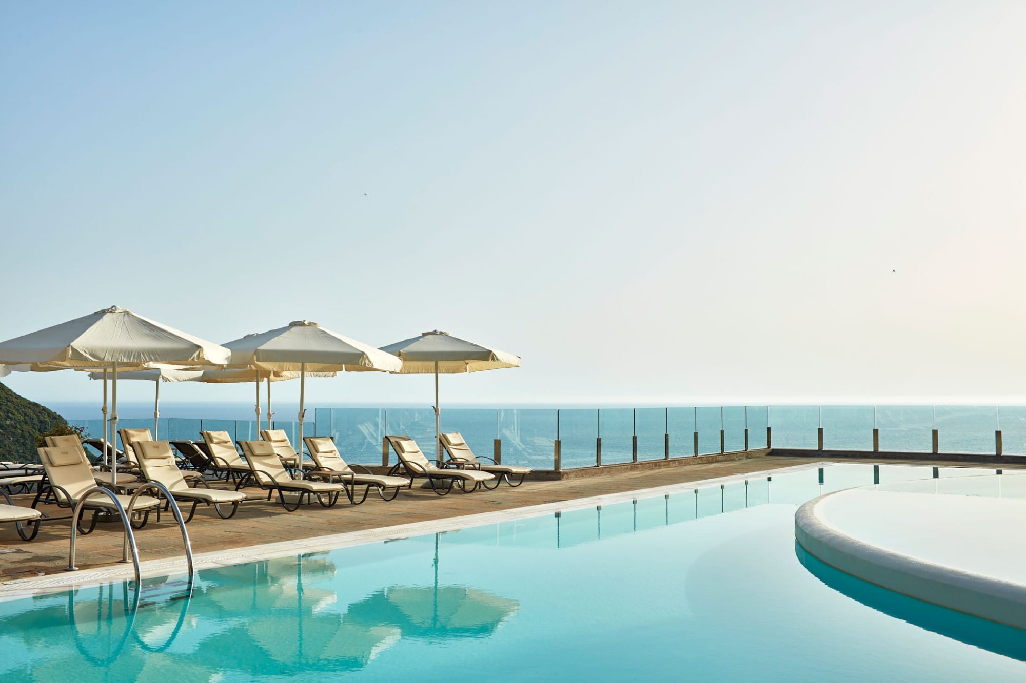 a pool with chairs and umbrellas by a beach