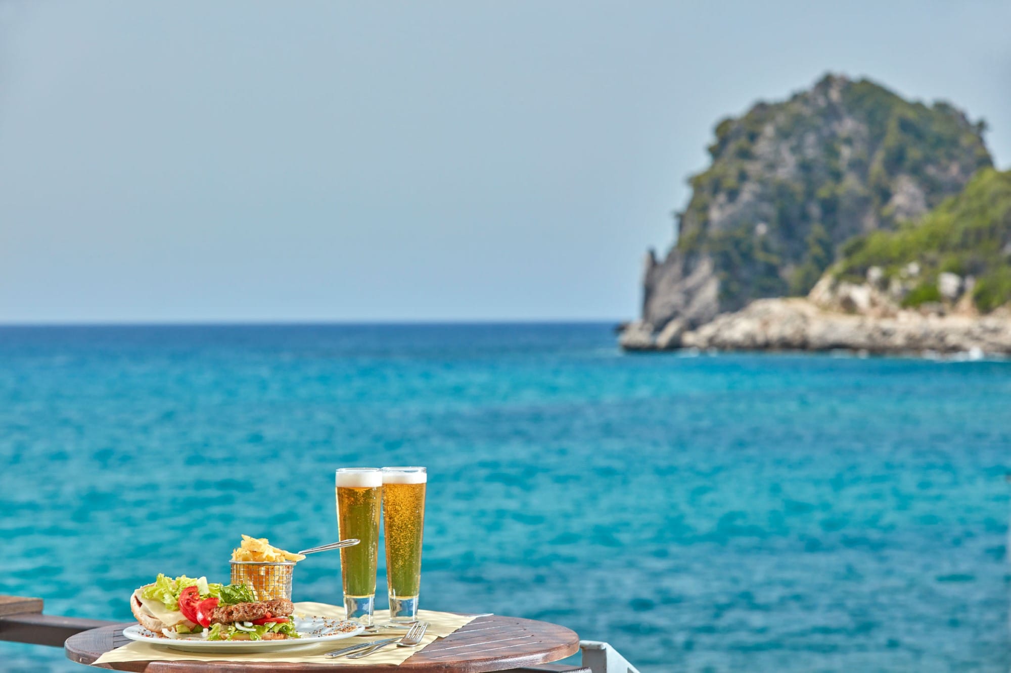 a table with glasses of beer on a dock by the water