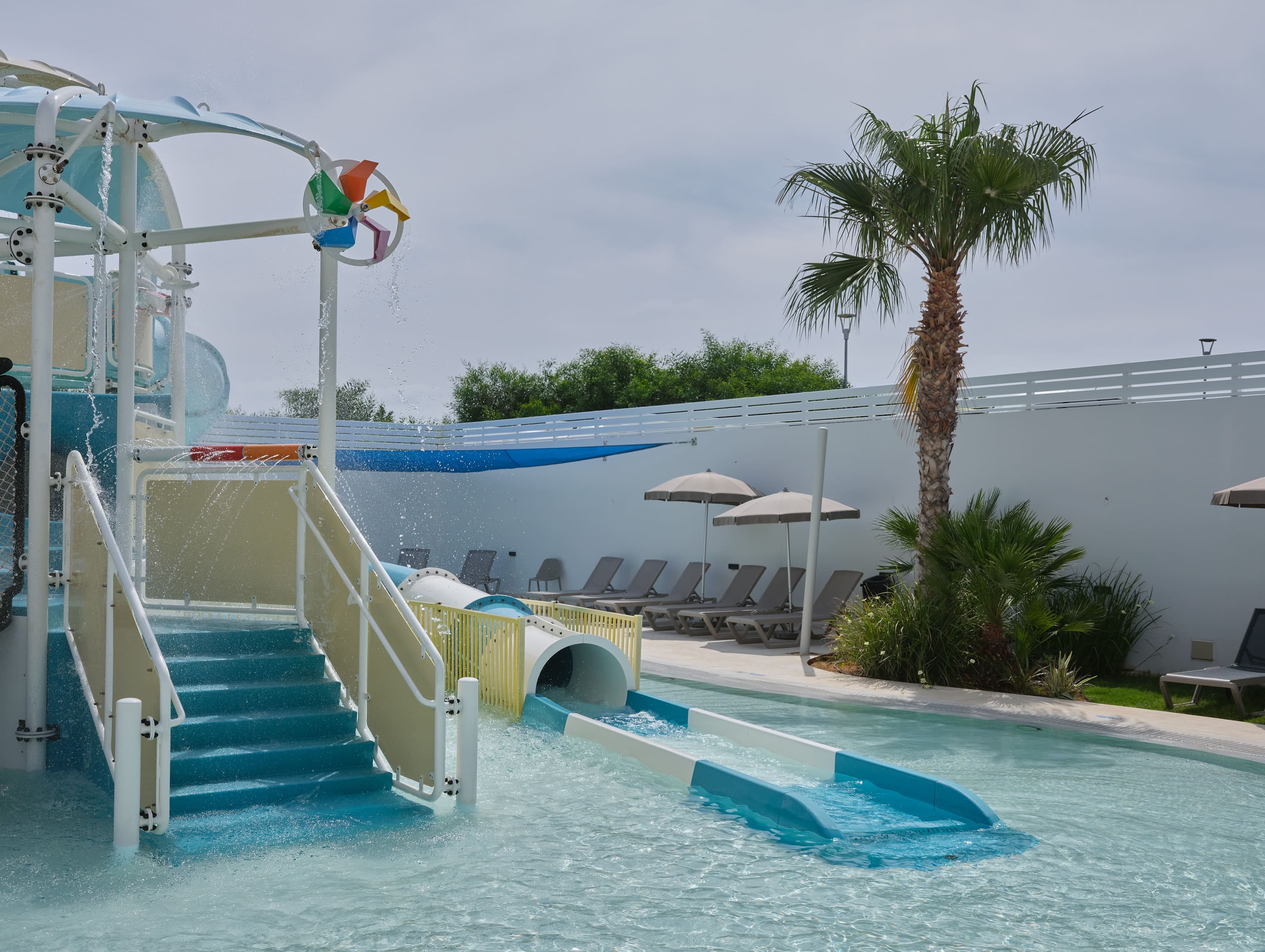 a pool with a slide and chairs by it by a beach
