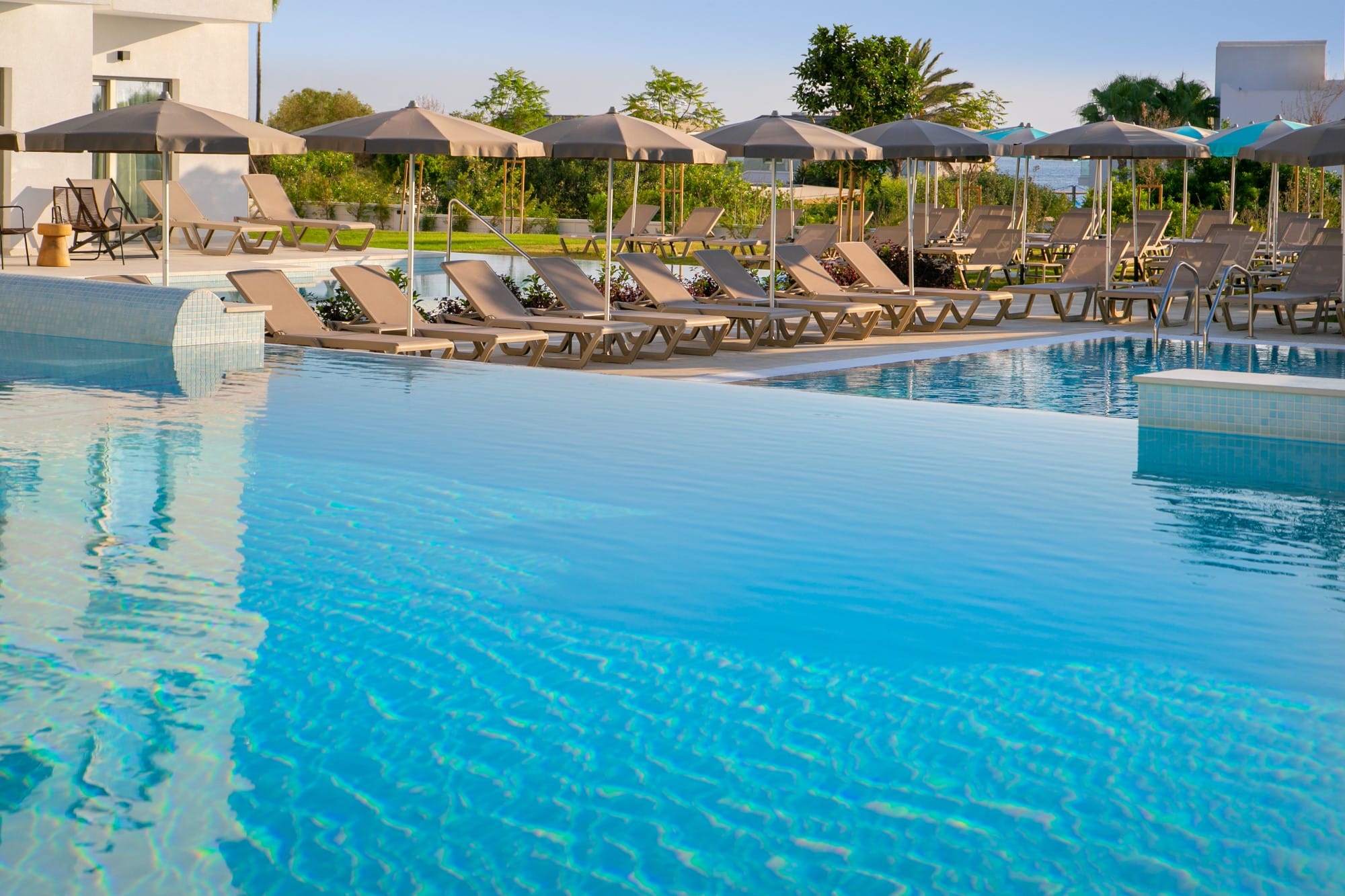 a pool with lounge chairs and umbrellas by a beach