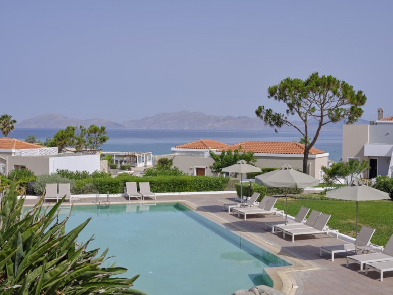 a pool with lounge chairs and umbrellas by a building and a body of water