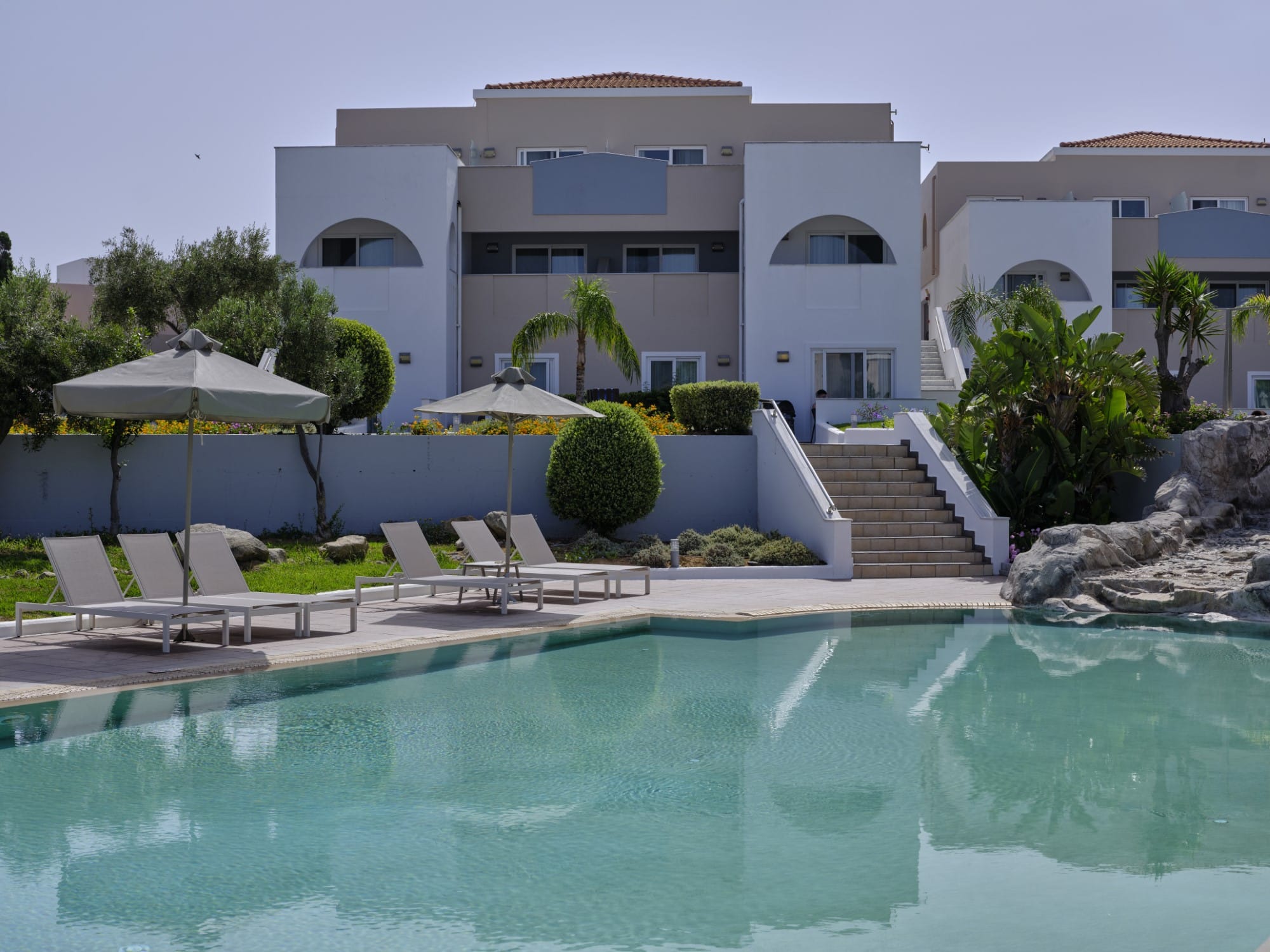 a pool with chairs and umbrellas by a building