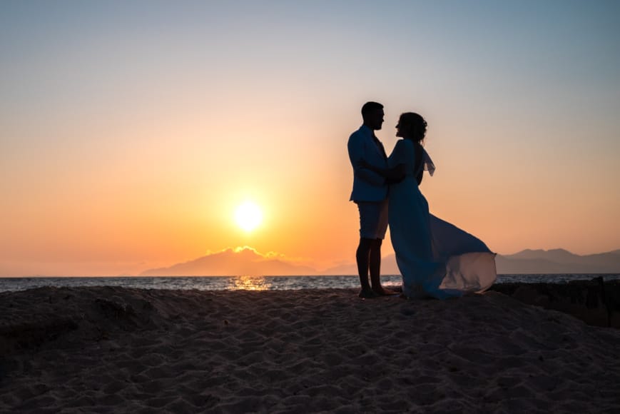 a man and woman holding hands on a beach at sunset