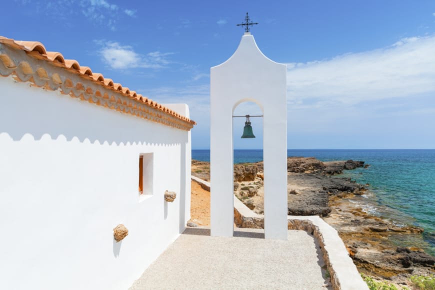 a white building with a cross on top of it by the water