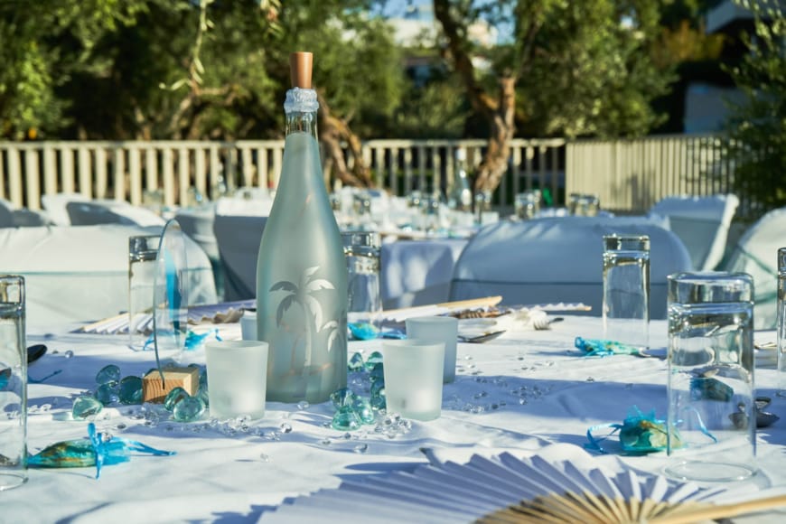 a table with chairs and a bottle on it with a table and a pool in the background