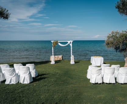a group of white chairs on a grassy hill by the water