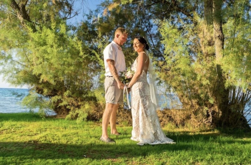 a man and woman standing in a grassy area with trees and water in the background