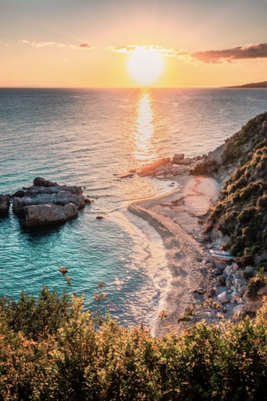 a beach with rocks and a body of water with a sunset