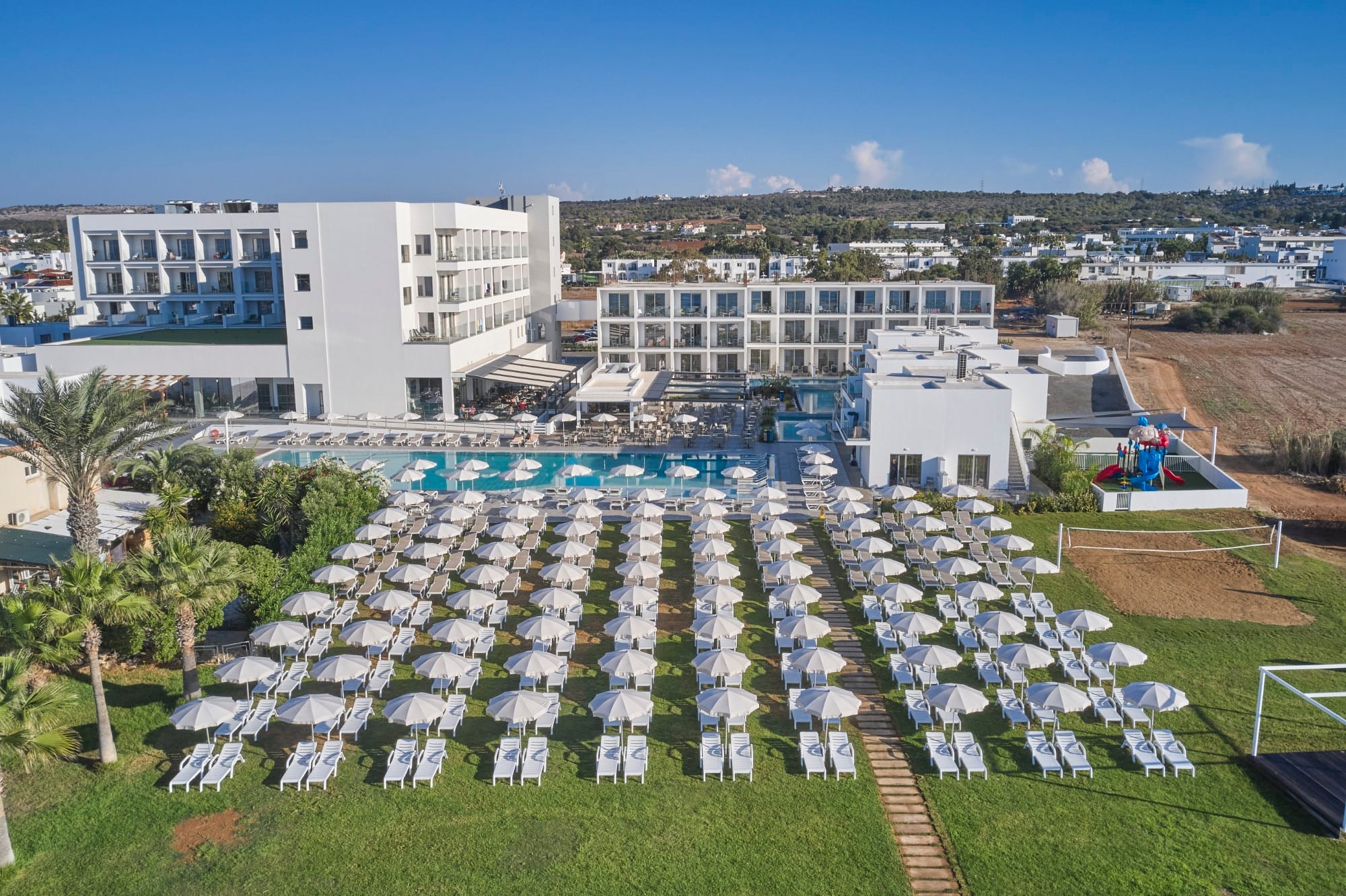 a large group of white chairs in a grassy area with buildings in the background