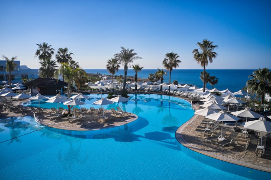 a pool with umbrellas and chairs by a beach