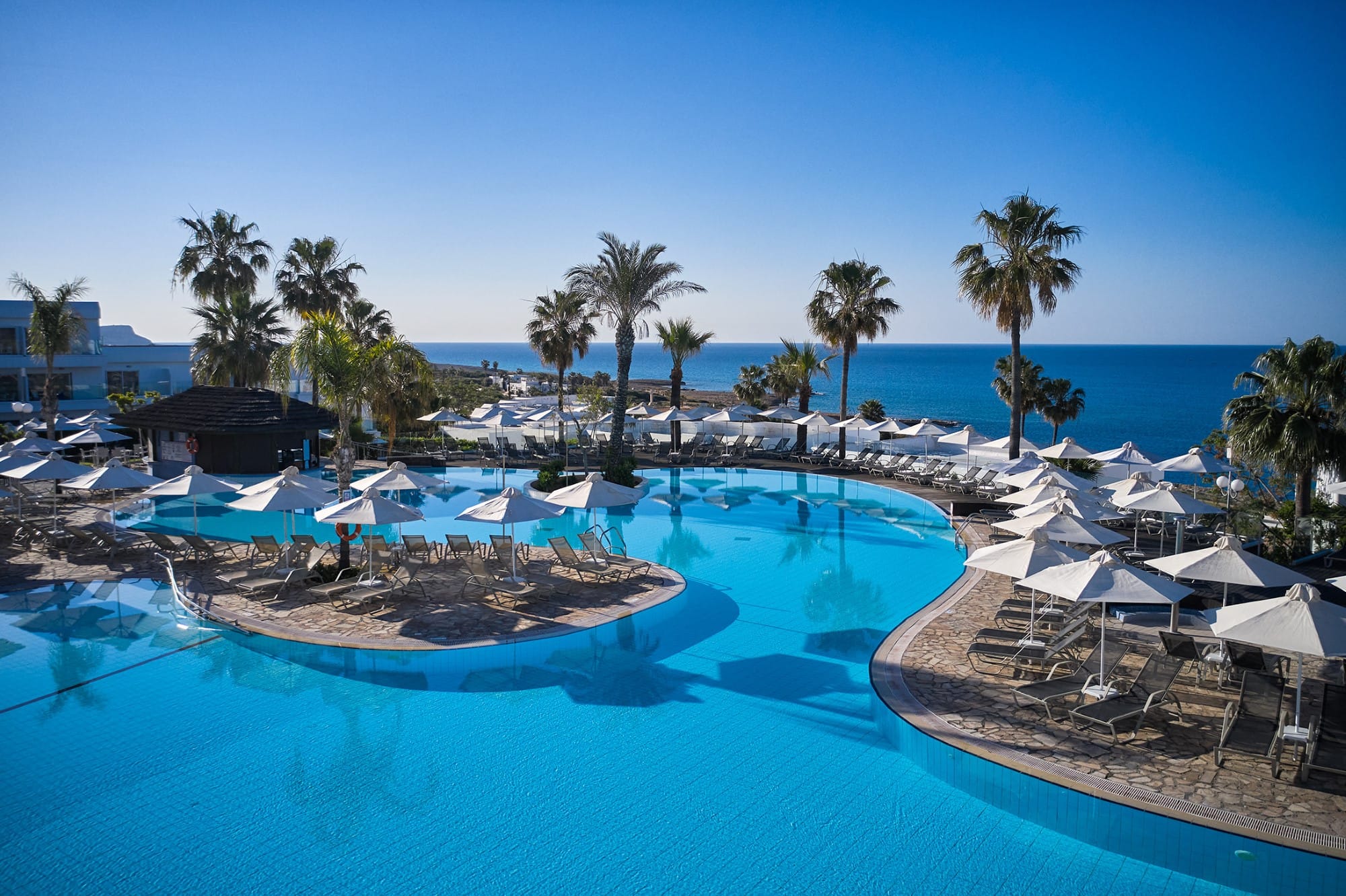 a pool with umbrellas and chairs by a beach