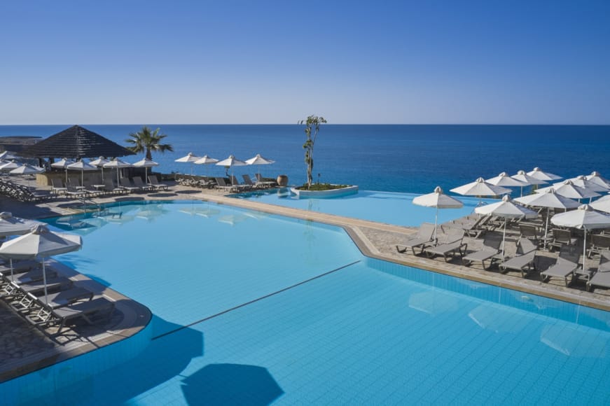 a pool with umbrellas and chairs by a beach