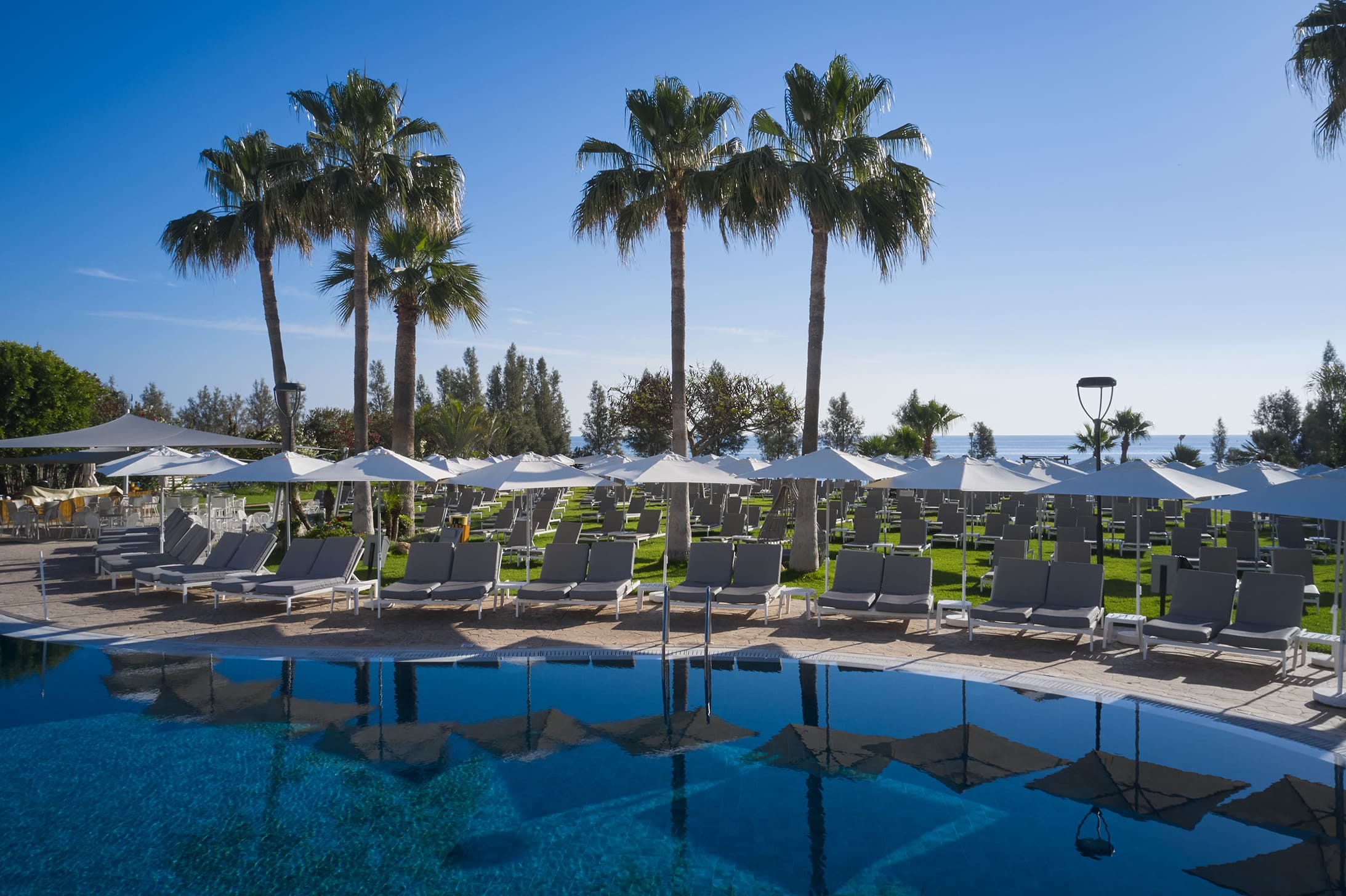 a pool with lounge chairs and umbrellas by a beach