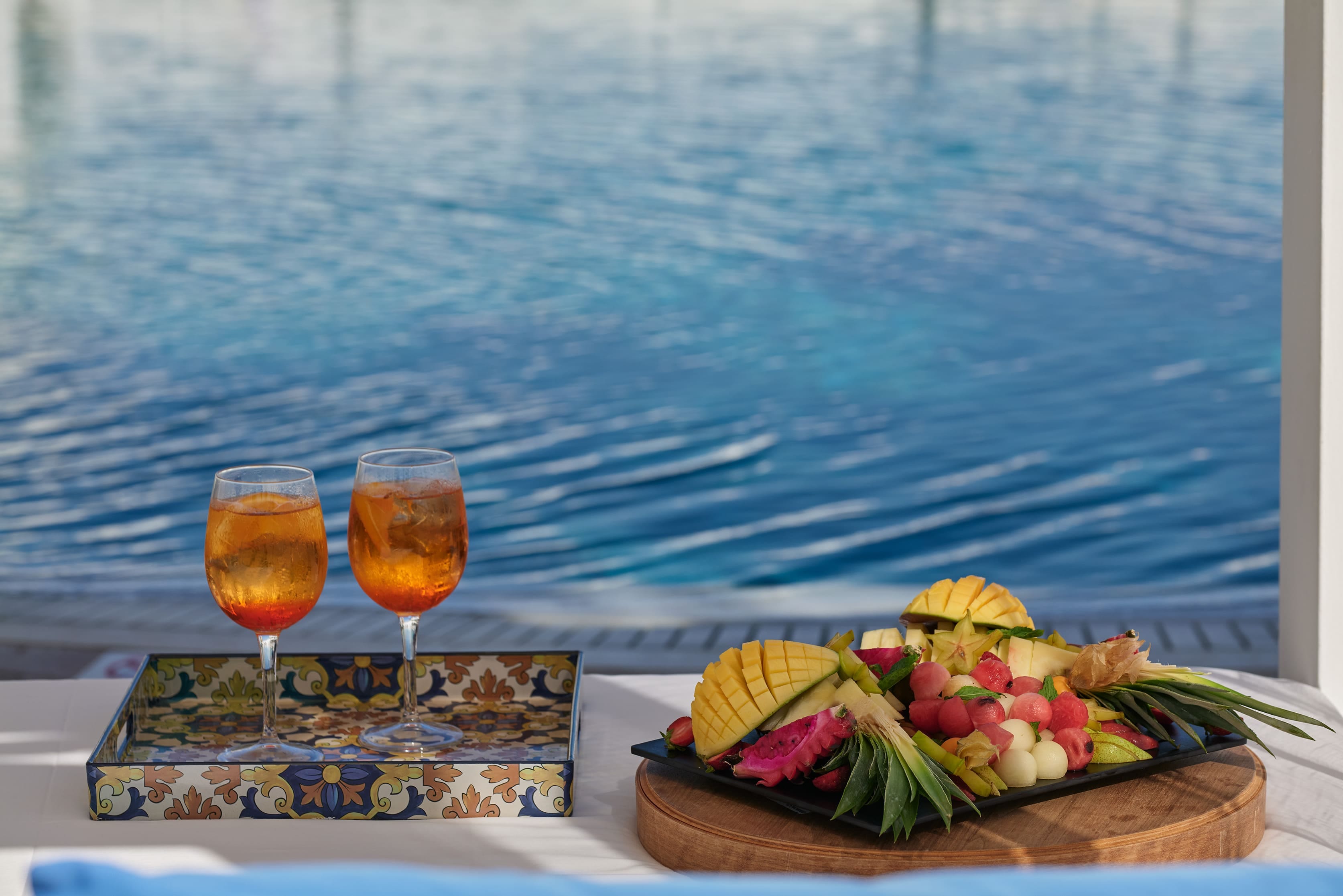 a basket of fruit and a glass of wine on a table by a body of water
