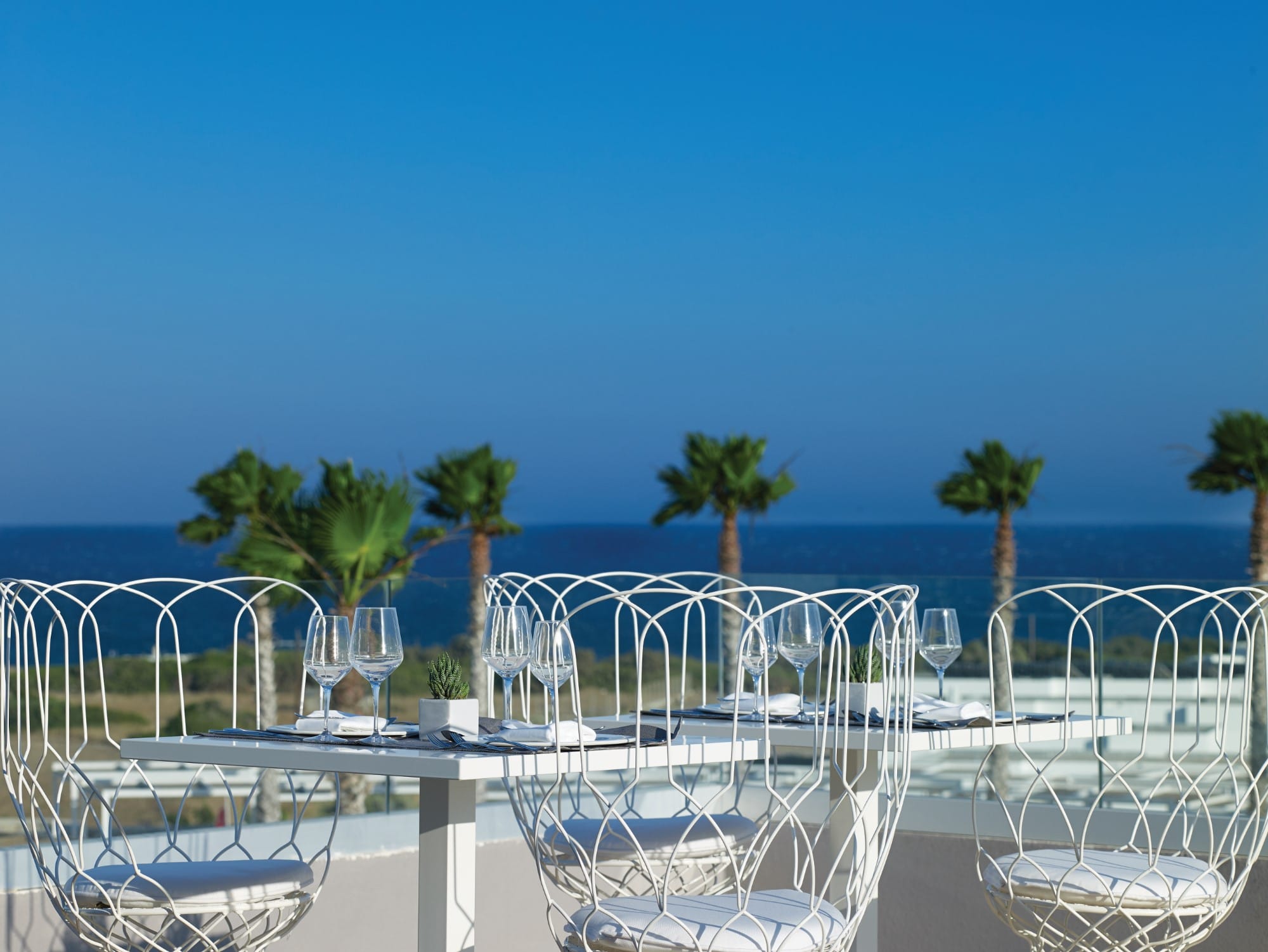a table with chairs and glasses on it by a body of water