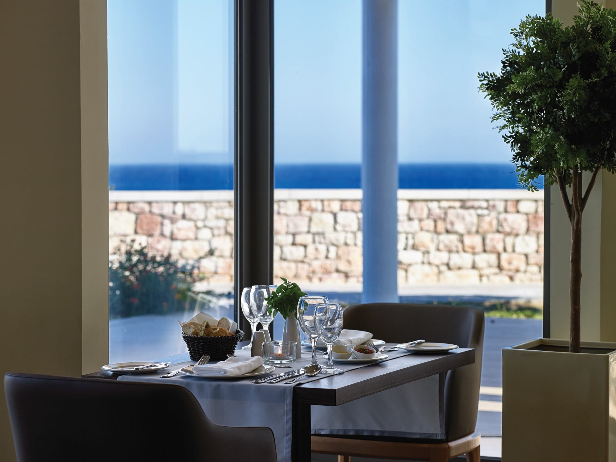 a table with glasses and plates on it by a window with a view of the ocean