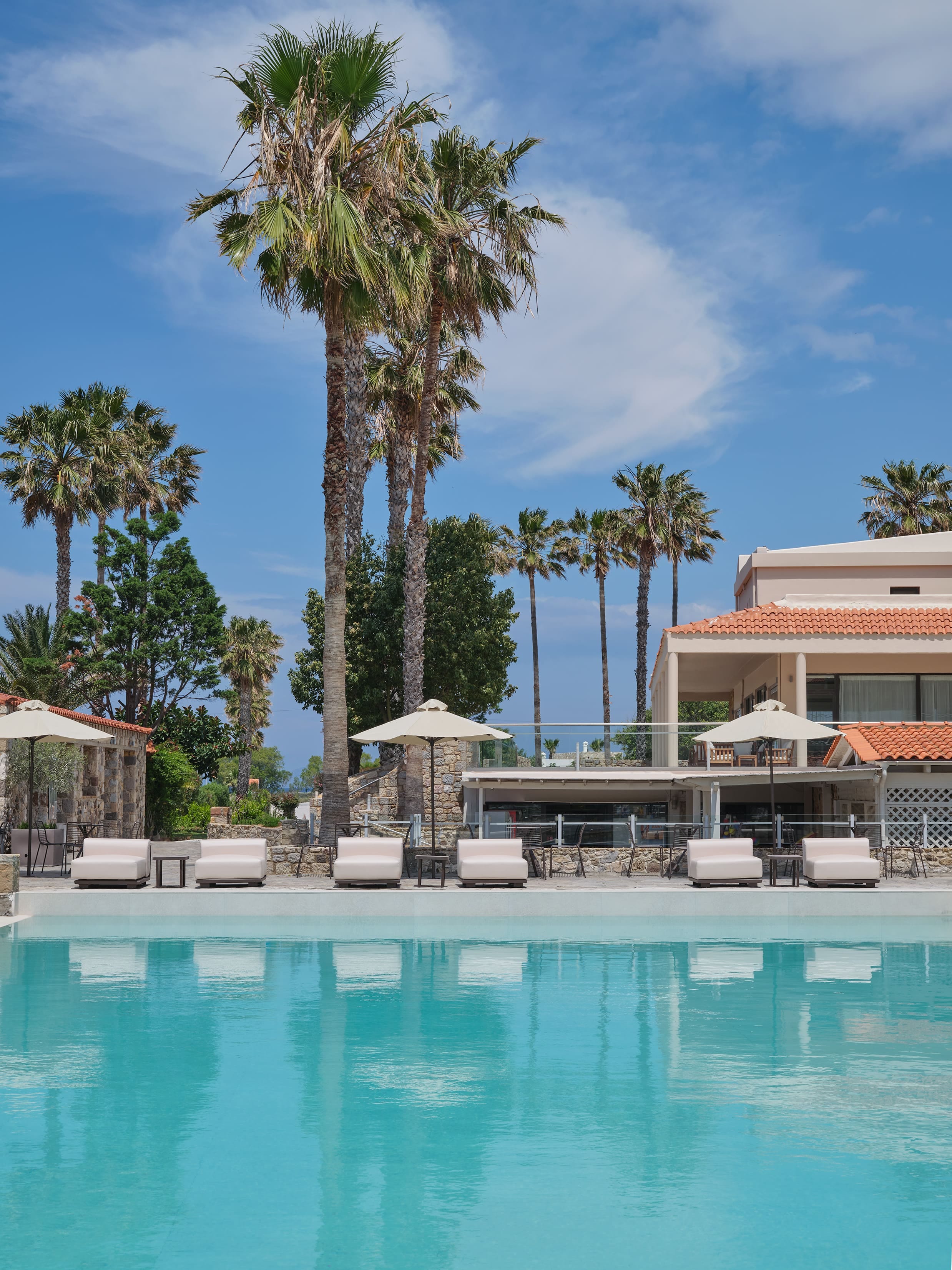 a pool with lounge chairs and umbrellas by a building and trees