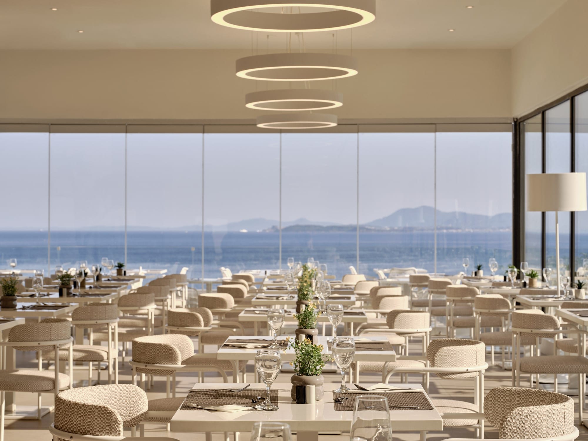 a room with tables and chairs and a body of water in the background