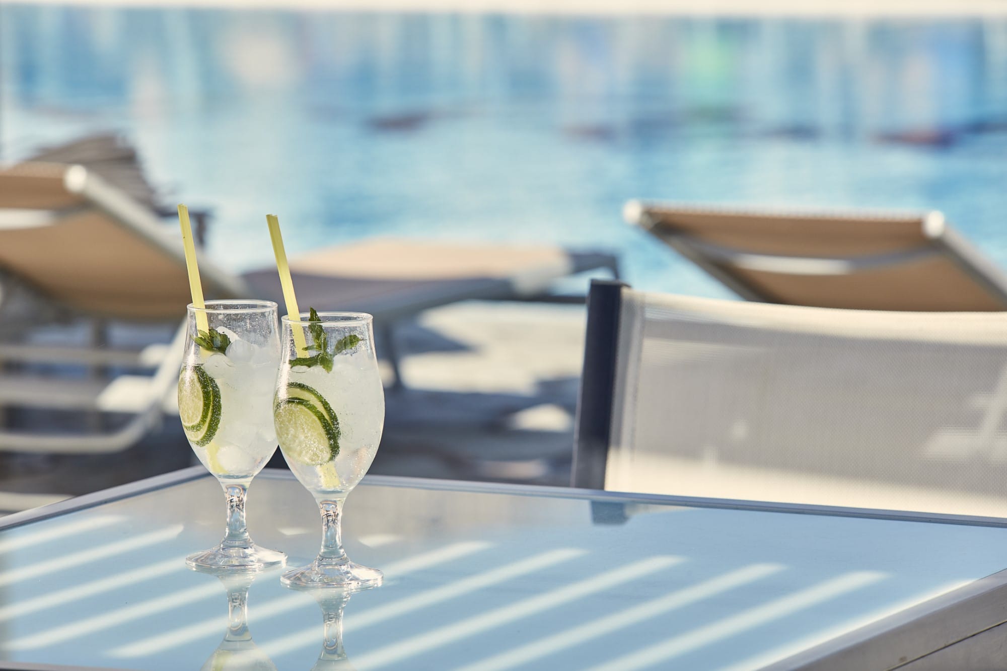 a couple of glasses with drinks on a table by a pool