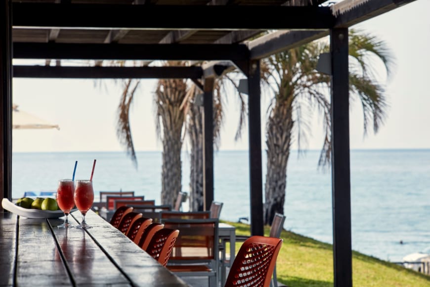 a table with drinks on it by a beach with palm trees