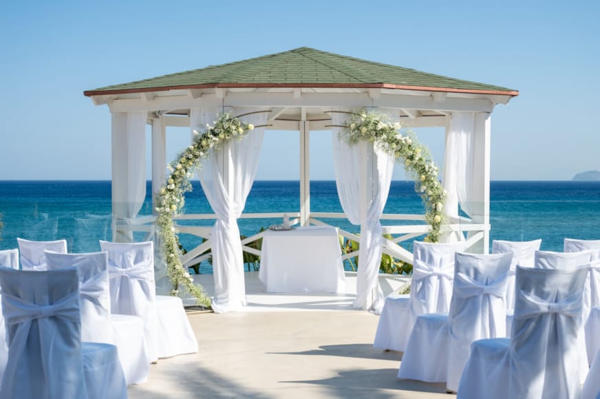 a group of white chairs and a gazebo on a beach