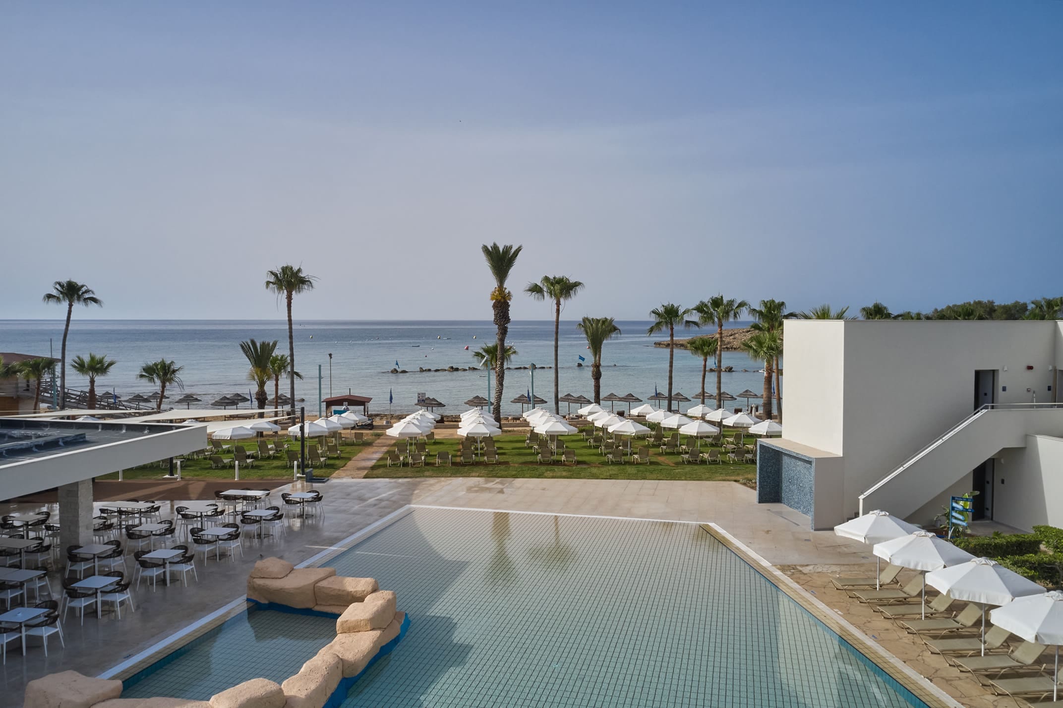 a pool with chairs and umbrellas by a beach