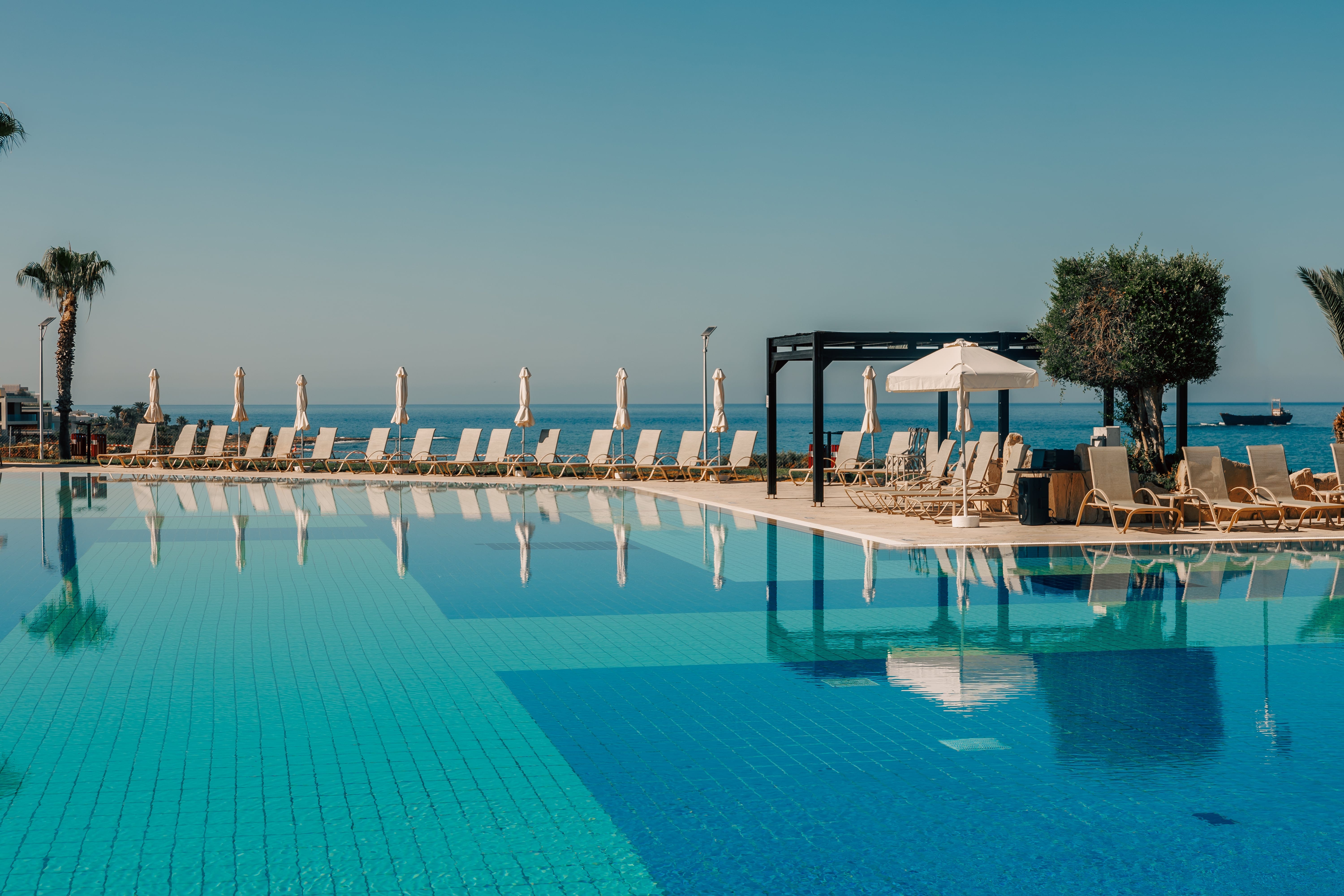 a pool with chairs and umbrellas by a beach
